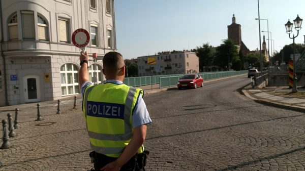 Ein Polizeibeamter hat die Polizeikelle erhoben um ein Fahrzeug anzuhalten.